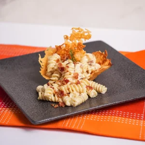 Plato de Fusilli a la Carbonara con salsa Alfredo, decorado con queso parmesano rallado y trozos de tocineta.